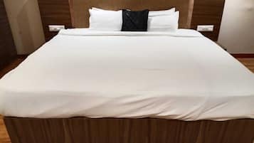 A bed with a wooden headboard, white bedding, and a dark accent pillow.