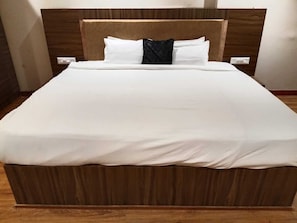 Una cama con cabecera de madera, ropa de cama blanca y un cojín decorativo oscuro.