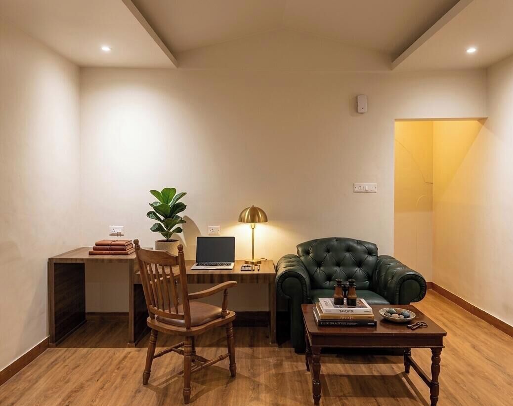 A room with a desk, a chair, a green sofa, a lamp, and a small table with books and a decorative item.
