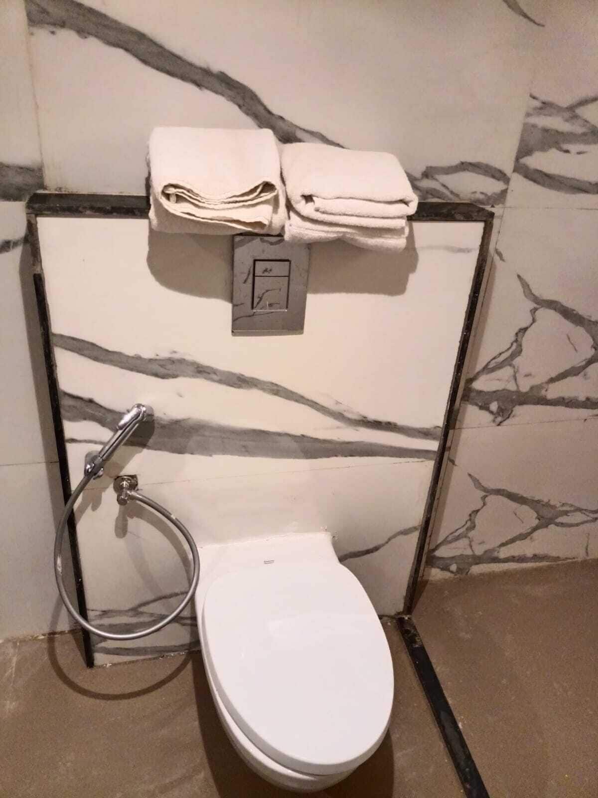A bathroom with a white toilet, a towel rack with folded towels, and a shower head.