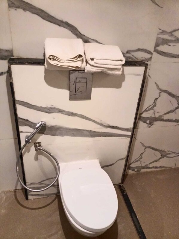 Un baño con inodoro blanco, un perchero con toallas dobladas y un cabezal de ducha.