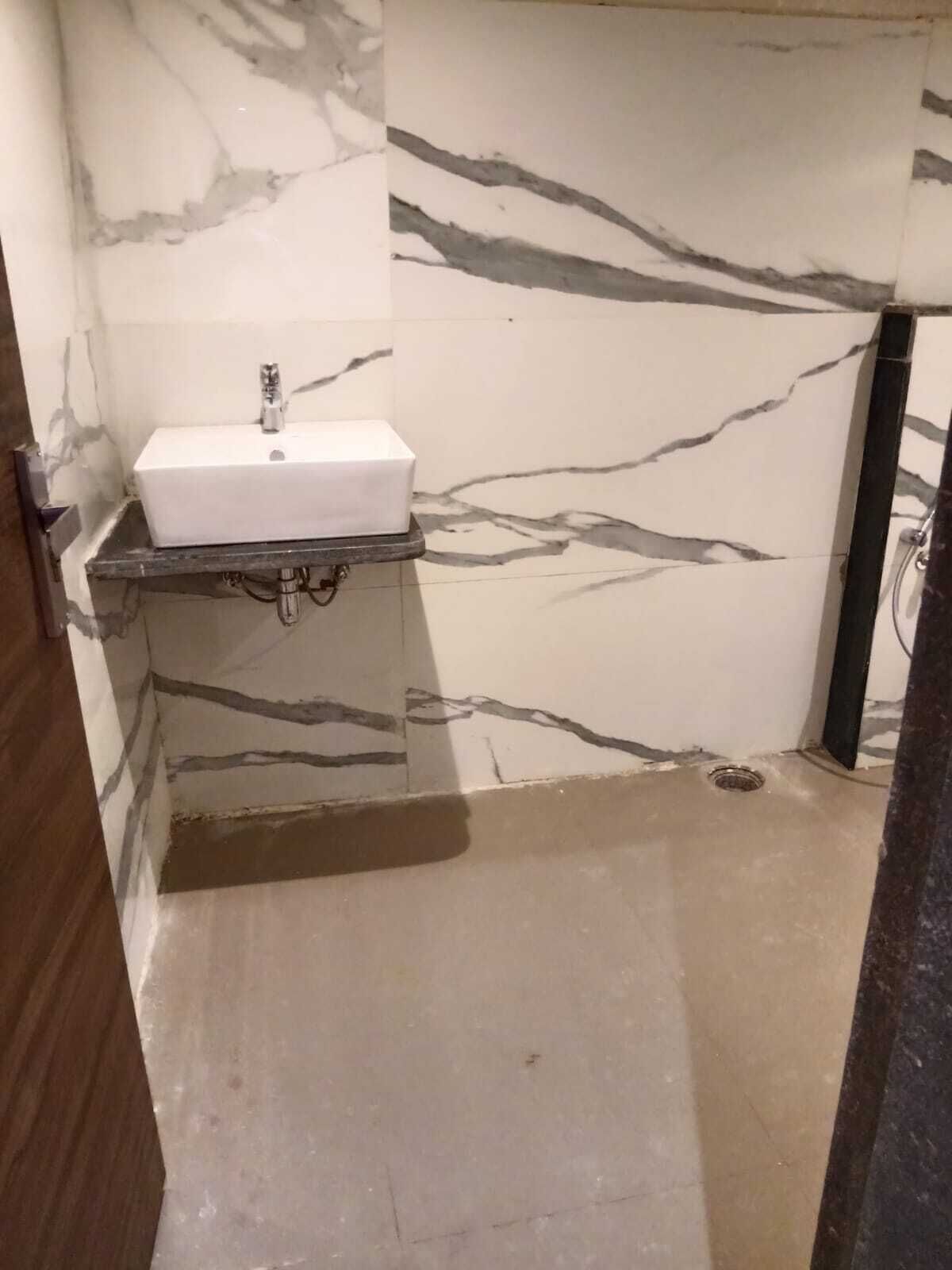A bathroom with a marble wall, a white sink, and a shower area.