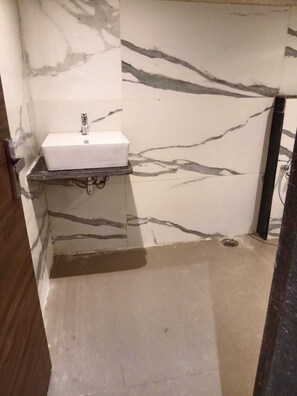 Un baño con pared de mármol, un lavabo blanco y zona de ducha.