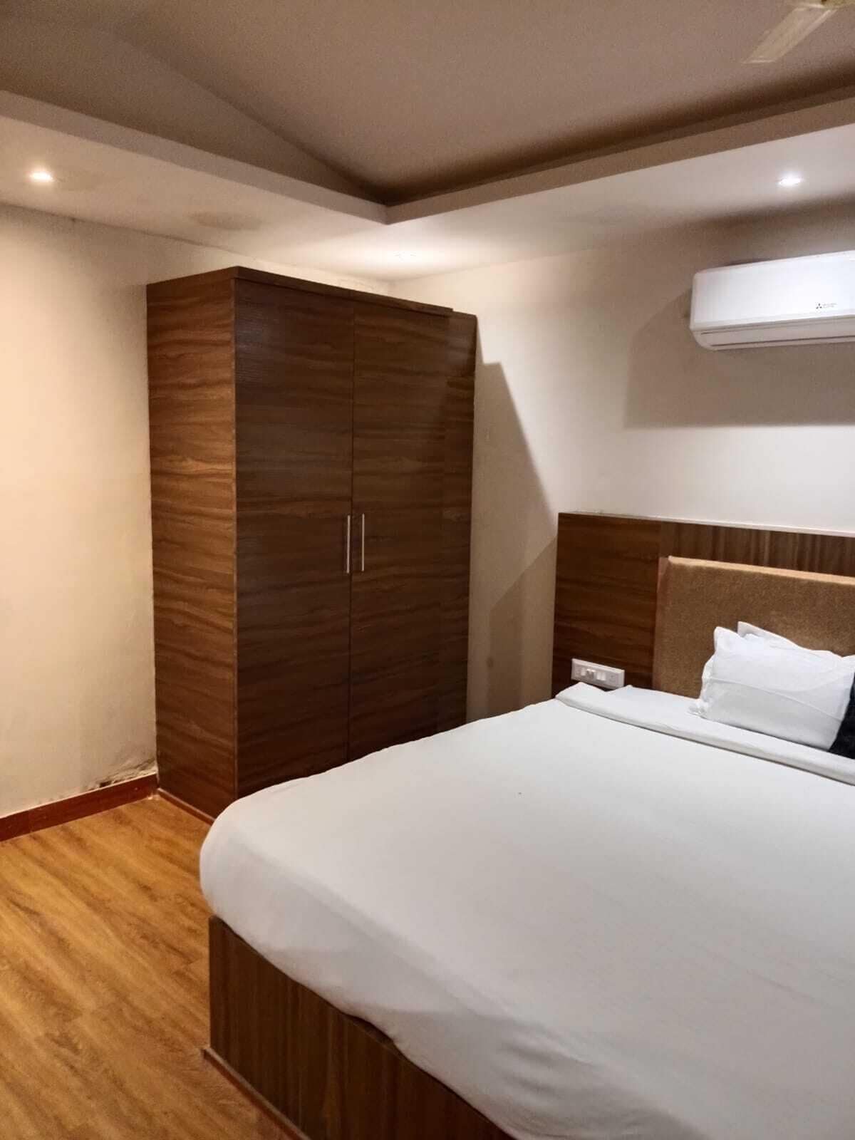 A hotel room with a large wardrobe, a bed with white bedding, and an air conditioning unit on the wall.