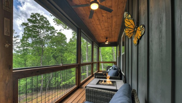 Eine überdachte Veranda mit Feuerstelle, Sitzgelegenheiten und Blick auf den Wald.
