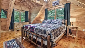 Ein Schlafzimmer einer Holzhütte mit einem Bett, einem Deckenventilator, einem Fenster und einem Nachttisch.