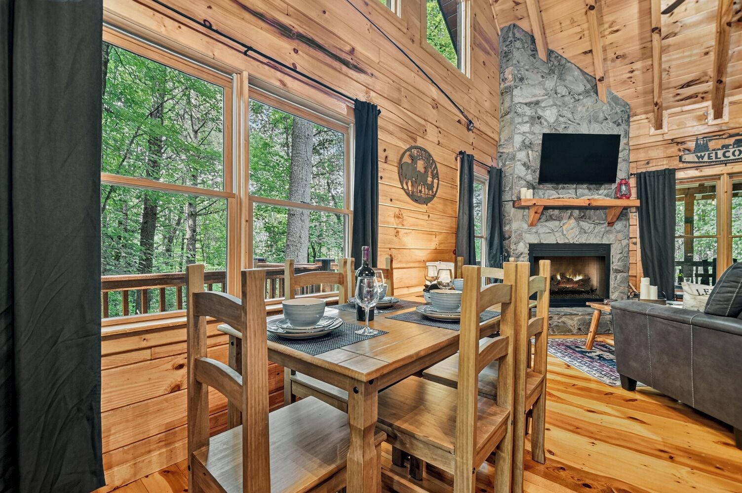 A wooden cabin interior with a dining table, chairs, a fireplace, and a sofa.