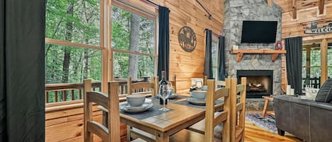 A wooden cabin interior with a dining table, chairs, a fireplace, and a sofa.