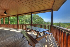A wooden deck with picnic tables, a railing, and a view of trees. - Private, dog-friendly cabin rental, tons of deck space, outdoor fireplace, hot tub (Morganton)