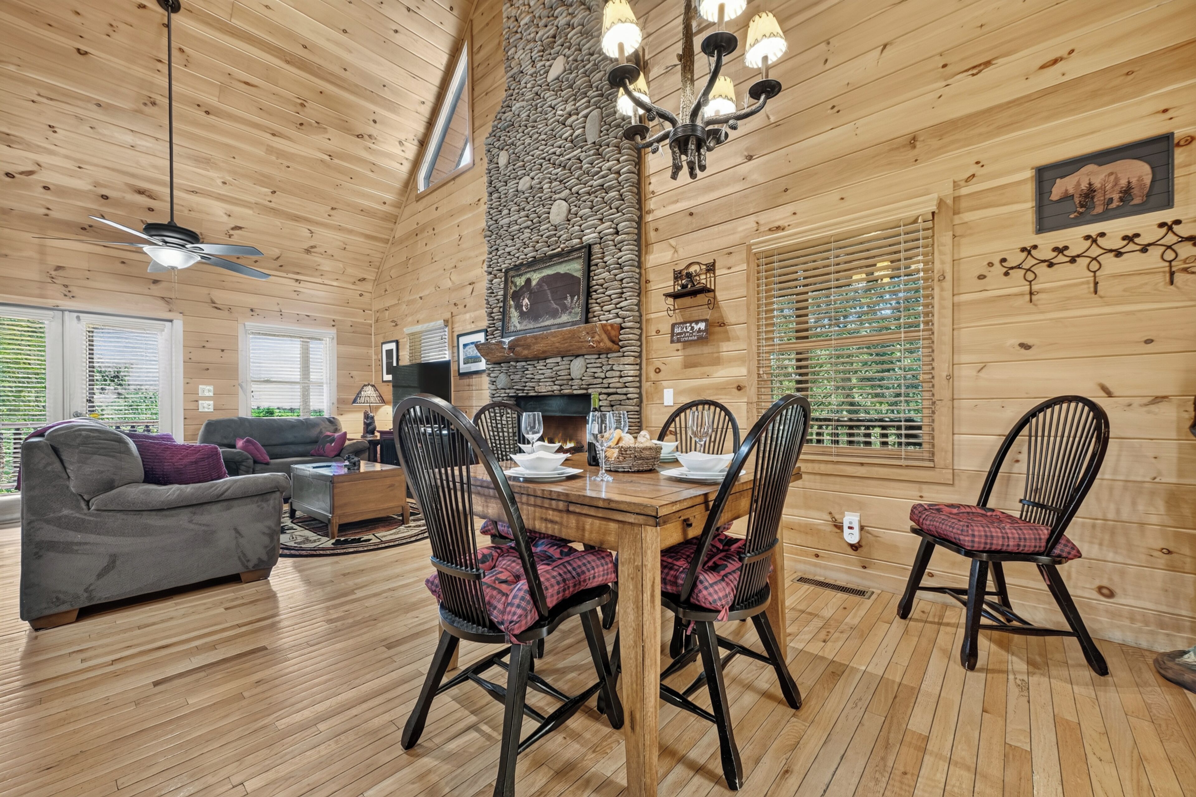 A wooden cabin interior with a dining area, fireplace, and a living room with a sofa and TV.