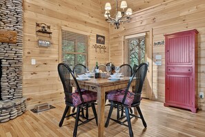 A wooden cabin interior with a dining table set for two, black chairs with plaid cushions, a chandelier, stone walls, and a red cabinet. - Private, dog-friendly cabin rental, tons of deck space, outdoor fireplace, hot tub (Morganton)