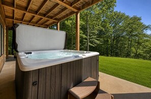 Un jacuzzi bajo una pérgola de madera, con césped y árboles al fondo.