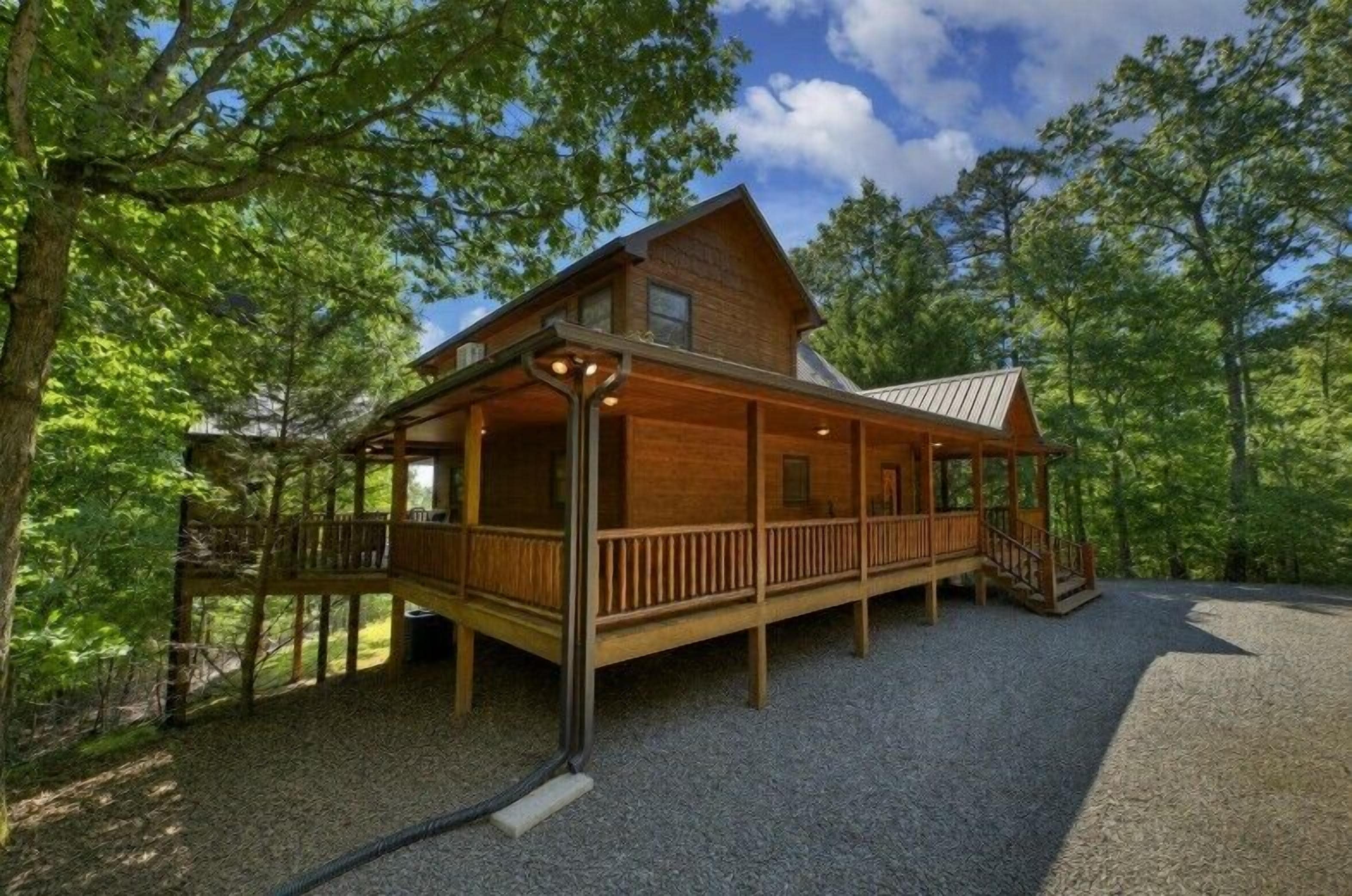 A wooden cabin with a porch, a covered deck, and a gravel driveway.