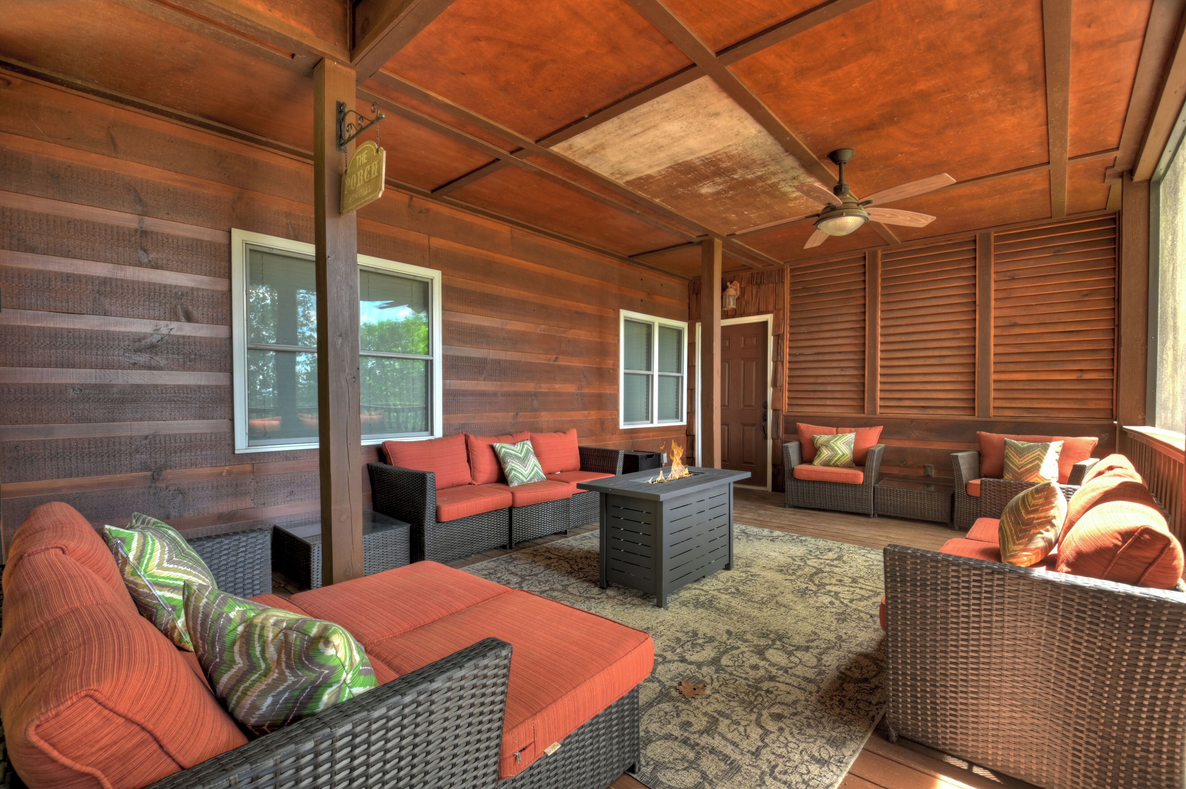 A covered outdoor seating area with wicker furniture, a fire feature, and a ceiling fan.