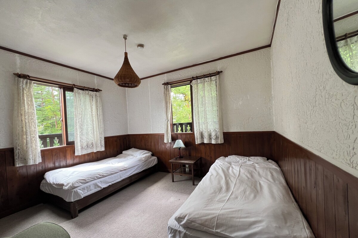 Une chambre avec deux lits simples, une petite table avec une lampe et une fenêtre avec des rideaux.