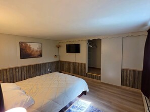 A bedroom with a bed, a flat-screen TV, a painting, and a wardrobe.