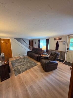 Un salon spacieux avec un plancher en bois, un canapé, un fauteuil et une lampe.