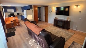 A modern living room with a sofa, TV, and kitchen in the background. - Birch Bungalow - Unit D a cozy 2-bedroom retreat in charming Sault Ste. Marie! (Sault Ste. Marie)