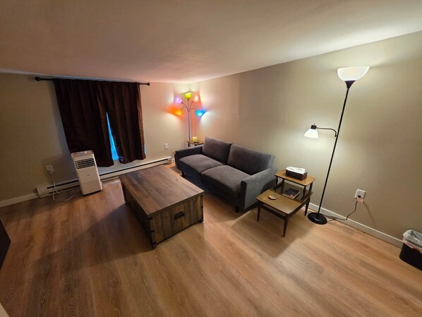 Un salon comprenant un canapé, une table basse en bois, un lampadaire et un radiateur.