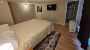A bedroom with a bed, a flat-screen TV, a heater, and a door leading to another room. - Birch Bungalow - Unit D a cozy 2-bedroom retreat in charming Sault Ste. Marie! (Sault Ste. Marie)