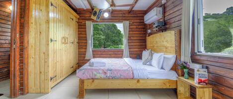 Un dormitorio de cabaña de madera con cama, ventana, ventilador de techo y una mesita de noche con un libro.