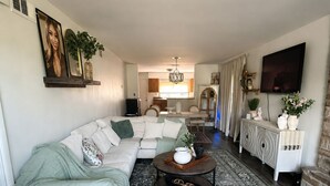 Uma sala de estar com sofá seccional, mesa de centro, tapete estampado, televisão e lareira.
