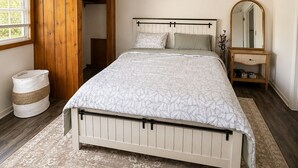 Quarto com cama, guarda-roupa de madeira, espelho e janela.