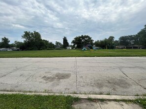 Un grand parking désert, avec une aire de jeux en arrière-plan.