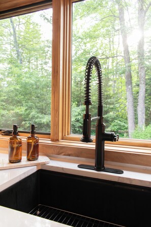 Una cocina con ventana, un grifo y dos botellas sobre la encimera.