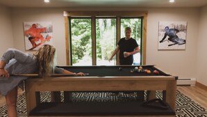 Un tavolo da biliardo in una stanza con pavimento decorato, una finestra vista alberi e due opere d'arte a tema sport appese al muro.