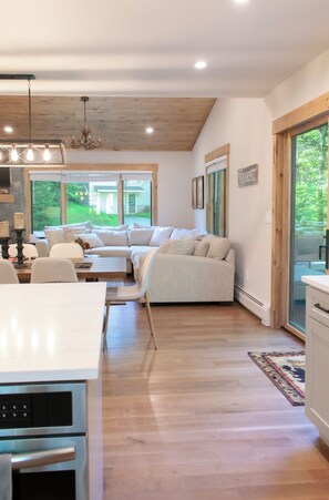 Una sala de estar moderna con un sofá seccional, un comedor y una cocina con electrodomésticos integrados.