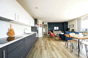 A modern kitchen with dark cabinets, a wooden cutting board, and a dining area with a table and chairs. - The London Horizon (London)