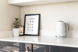 Un taulell de cuina amb un gràfic de cafè emmarcat, una paperera blanca i una planta en test.