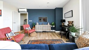 En moderne stue med en blå accentvæg, et konsolbord i midten, en sofa, en rød lænestol og et tæppe med et mønster.