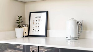 En køkkenbordplade med et indrammet kaffediagram, en hvid elkedel og en potteplante.