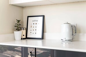 Eine Küchenarbeitsplatte mit einer gerahmten Kaffeetafel, einem weißen Wasserkocher und einem Blumentopf.