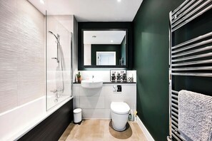 A modern bathroom with a glass shower enclosure, a white sink, a toilet, and a towel rack. - The London Horizon with Air-con (London)