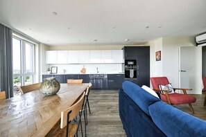 A modern kitchen with white cabinets, a dining table with chairs, a blue sofa, and a red armchair. - The London Horizon with Air-con (London)