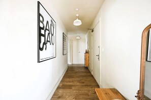 A hallway with wooden flooring, white walls, and framed artwork. There is a wooden bench and a mirror on the right. - The London Horizon (London)