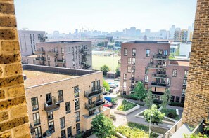 A view of a residential area with multi-story brick buildings, balconies, and a green space with trees. - East London Views - Modern Apartment (Greater London)