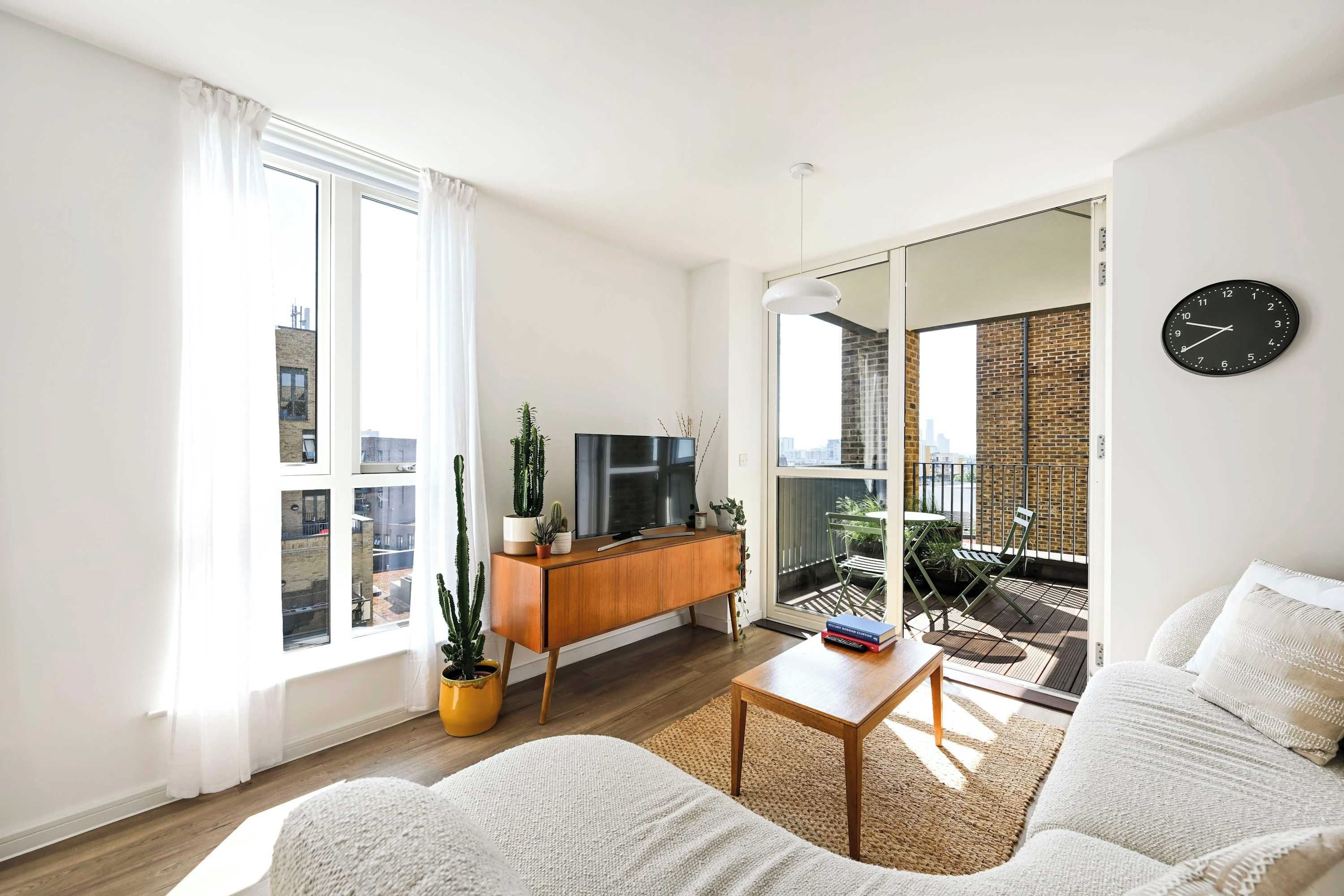 A modern living room with a sofa, a coffee table, a TV on a wooden cabinet, and a balcony with a view.