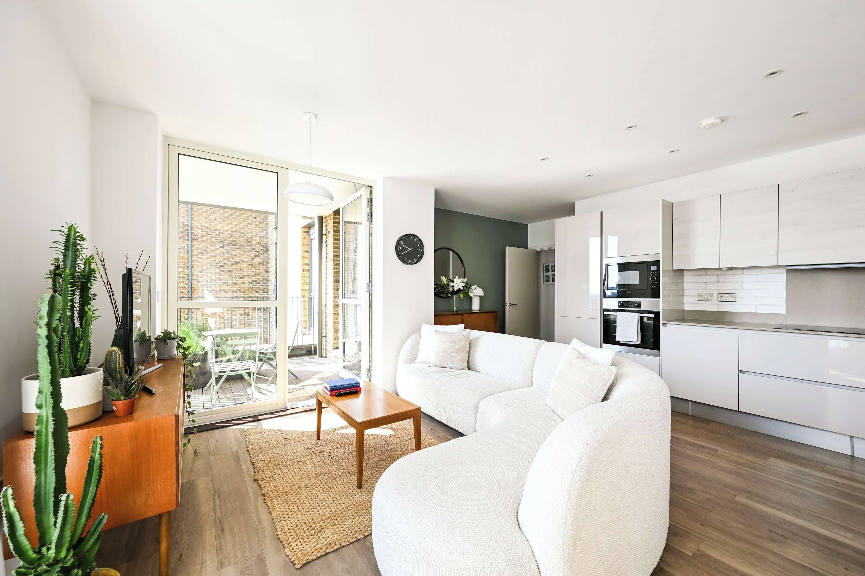 A modern living room with a white sofa, a wooden coffee table, and a cactus plant on a wooden console.