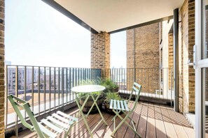 A balcony with a table and chairs, potted plants, and a view of the cityscape. - East London Views - Modern Apartment (Greater London)