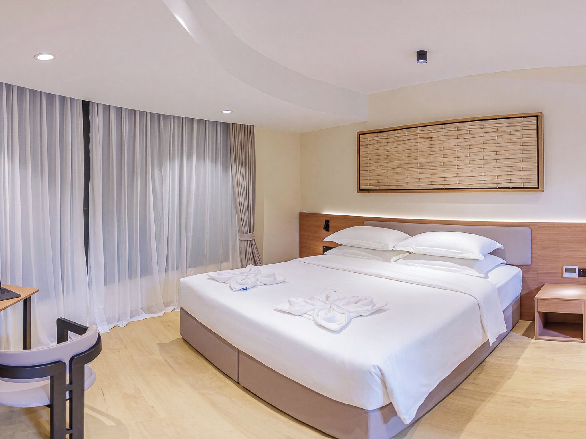 A hotel room with a large bed, a bedside table, a desk with a chair, and a wall-mounted artwork.