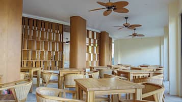 A spacious indoor area with multiple wooden tables and chairs, ceiling fans, and a wooden bookshelf.