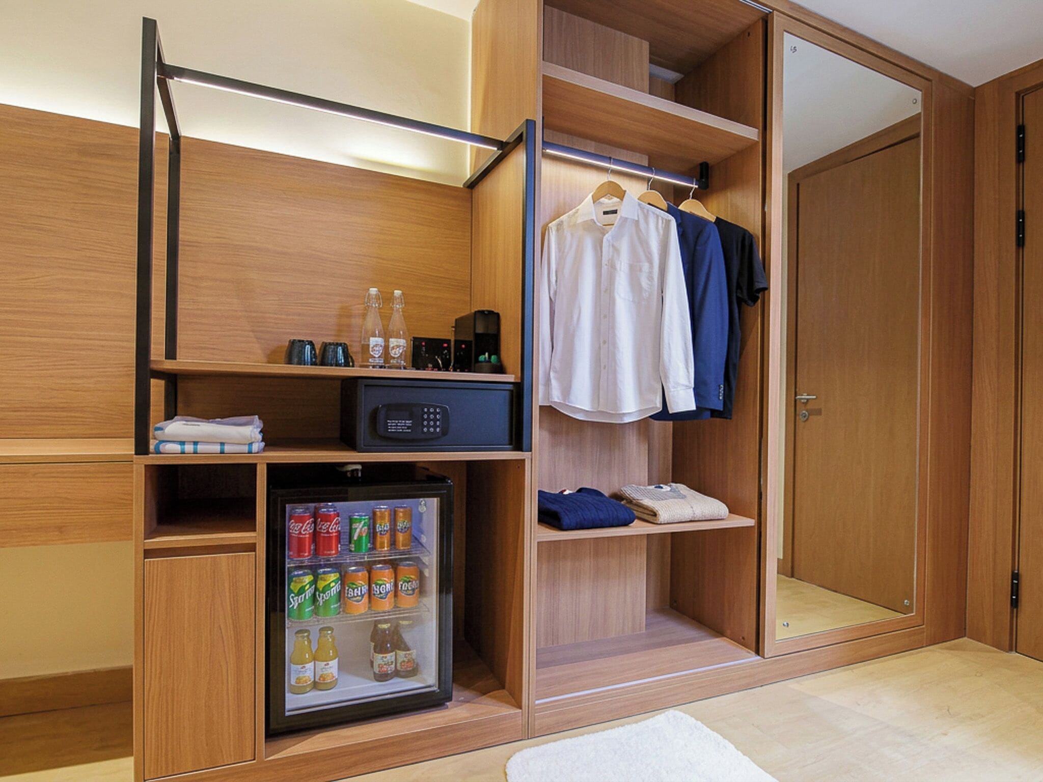 A walk-in closet with a built-in refrigerator, shelves with beverages, and hanging clothes.