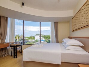 A hotel room with a large bed, a desk, and a view of the cityscape. - Kinan Sentral Maldives (Fulidhoo)