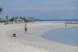 Una playa con cielos despejados, palmeras y algunas personas.