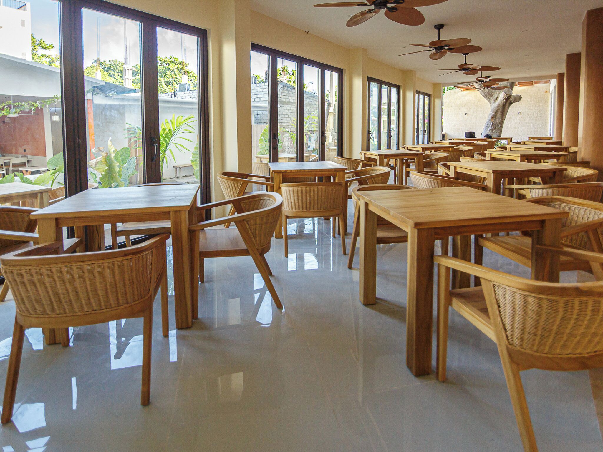 A spacious dining area with multiple tables and chairs, large windows, and ceiling fans.