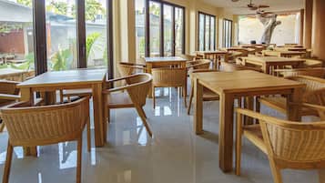 A spacious dining area with multiple tables and chairs, large windows, and ceiling fans.